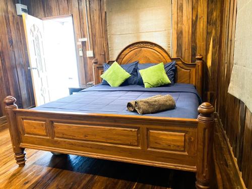 a large wooden bed with blue sheets and green pillows at Ban Tidlay - SHA in Ko Yao Noi