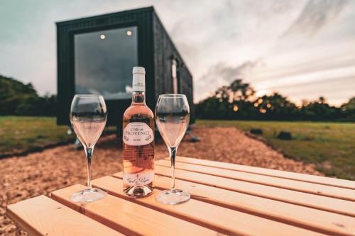 Una botella de vino y dos copas de vino en una mesa de madera. en OffGrid Tiny Home W/ View Of South Downs NP en Petersfield