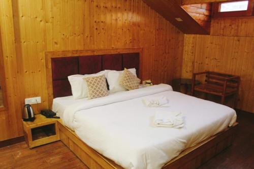 a bedroom with a large white bed with wooden walls at Hotel White Cloud in Banikhet