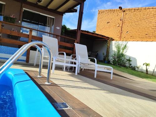 a pool with white chairs next to a house at Chalés aconchegantes em Boituva in Boituva