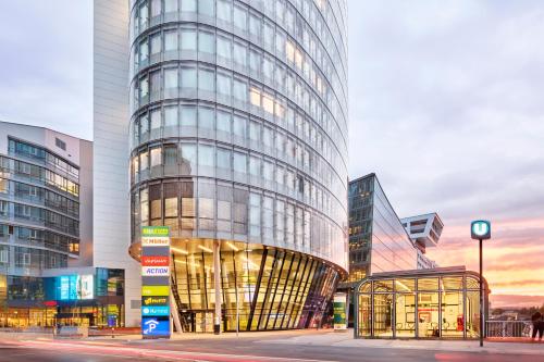 un edificio de cristal alto con una parada de autobús delante de él en H2 Hotel Wien Schönbrunn en Viena