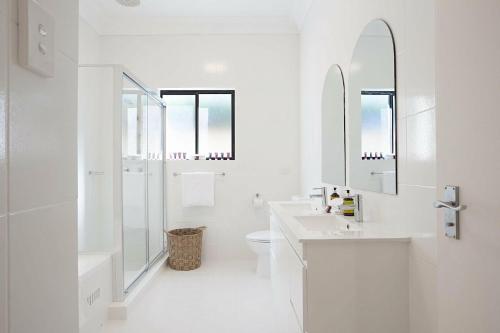 a white bathroom with two sinks and a toilet at Coastal Tamarama in Sydney