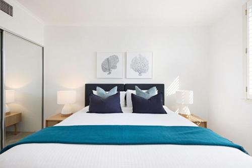 a white bedroom with a large bed with blue pillows at Palm Breeze in Coogee in Sydney
