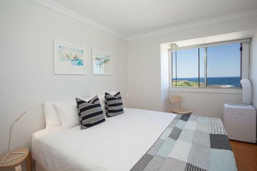 a white bedroom with a bed with a view of the ocean at Ocean view Clovelly in Sydney