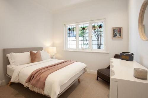 a white bedroom with a bed and a window at The Cali Beach house Bronte in Sydney