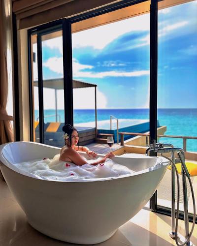 a woman laying in a bath tub in a room with the ocean at Angsana Velavaru in Dhaalu Atoll