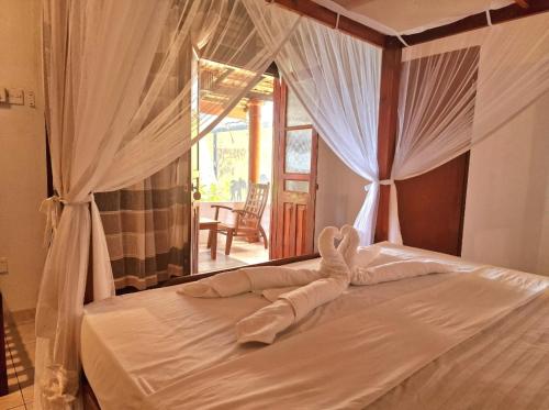Panorama Beach Hotel في تانجالي: غرفة نوم بسرير مع شراشف بيضاء وستائر
