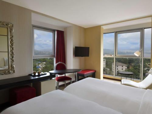 a hotel room with a bed and a desk and windows at Pullman Kinshasa Grand Hotel in Kinshasa