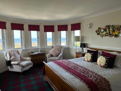 a bedroom with a bed and two chairs and windows at Beaches in Ayr