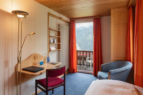 a hotel room with a desk and a chair and a window at Hotel Bellevue - Traditional Swiss Hideaway in Wengen