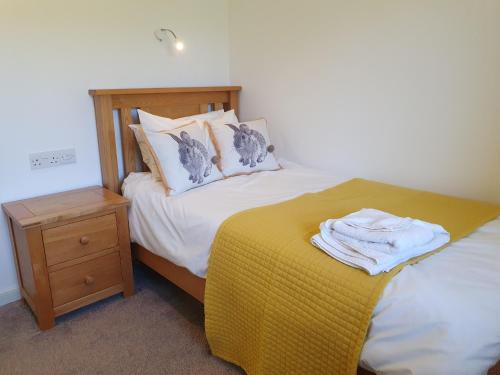 a bed with a yellow blanket next to a night stand at Woodwick Mill Cottage in Evie
