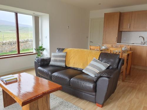 a living room with a leather couch and a table at Woodwick Mill Cottage in Evie