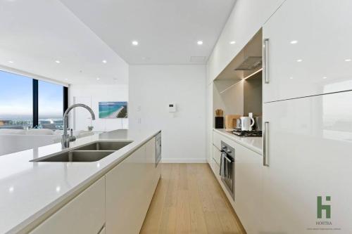 a white kitchen with white counters and a sink at St Leonards 2B2B Apt with Skyview in Sydney