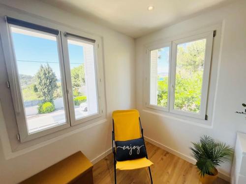 une chaise jaune dans une pièce avec trois fenêtres dans l'établissement Cosy Appartement Vue mer, Clim, Place de Parking, à Sanary-sur-Mer