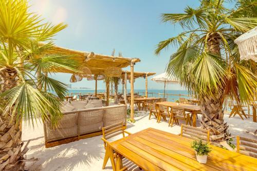 a restaurant on the beach with tables and palm trees at Mövenpick Resort Al Marjan Island in Ras al Khaimah