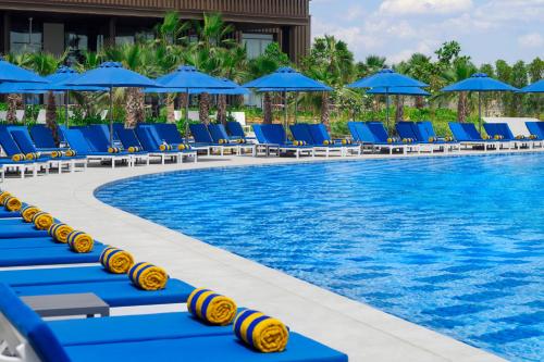 a pool with blue lounge chairs and blue umbrellas at Mövenpick Resort Al Marjan Island in Ras al Khaimah