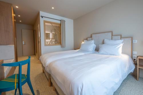 a bedroom with a large white bed and a blue chair at Hôtel Les Pins in Saint-Trojan-les-Bains
