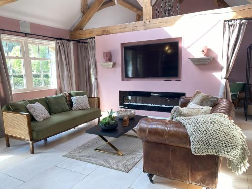 a living room with a couch and a television on a wall at Lynford Holiday Cottages nestled in the heart of Thetford Forest in Mundford