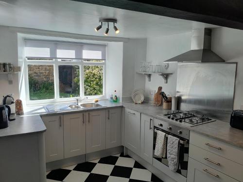 a kitchen with white cabinets and a stove and a window at Mews Cottage, a 2 bedroom Georgian Cottage which comfortably sleeps 4 located in a quiet courtyard in the centre of Olney in Olney