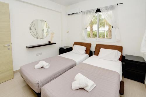 two beds in a room with white walls and a mirror at Villa Thetida in Ayia Napa