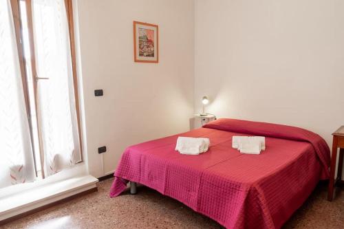 1 dormitorio con 1 cama roja y 2 toallas blancas en La casa dei fiori 10 min dal mare, en Fano