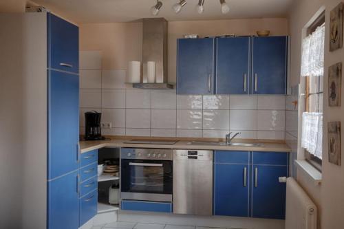 La cuisine est équipée de placards bleus et d'un four avec plaques de cuisson. dans l'établissement Ferienhaus Ziegler, à Loßburg