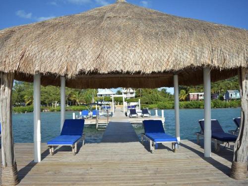 a pier with blue chairs and a straw umbrella at Sea Garden Cottage in Caye Caulker