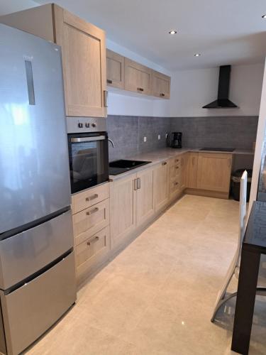 une cuisine avec des armoires en bois et un réfrigérateur en acier inoxydable dans l'établissement Gites des falaises de Longues 6personnes, à Longues-sur-Mer