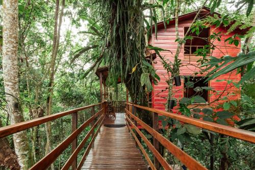 un puente de madera que conduce a una casa roja en el bosque en Tominejo Ecolodge Casas en los árboles, en Neira