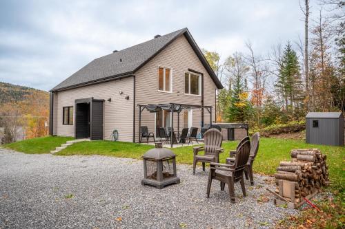 PohénégamookにあるLe Jarret Noir! Chalet NEUF en nature SPA/Vue Lacの椅子とグリルが前にある家