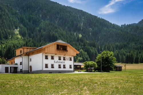 a building in a field in front of a mountain at Kahnwirt in Valle Di Casies