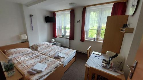 a bedroom with two beds and a desk and windows at Penzion PANORAMA Janovičky in Broumov