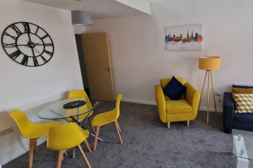 a living room with yellow chairs and a table and a clock at 2 Bedroom Penthouse in Coventry - Private Parking in Coventry