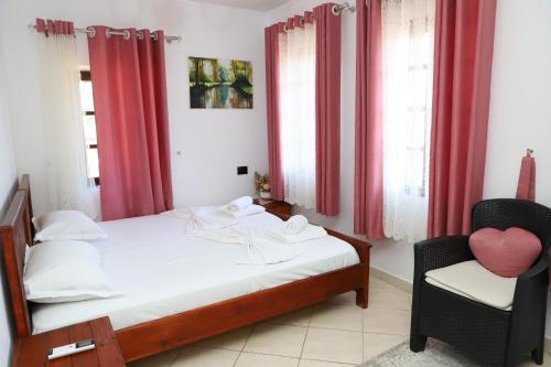uma cama e uma cadeira num quarto com cortinas vermelhas em Guest House LION em Berat