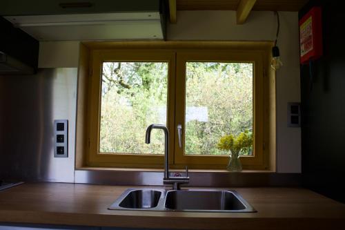 a kitchen sink with a window above a kitchen counter at Les Jours Heureux Tiny House in Villers-le-Gambon