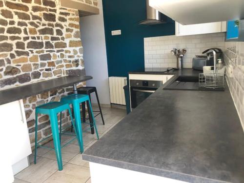 une cuisine avec des tabourets bleus et un mur en pierre dans l'établissement Maison de famille avec SPA, à Clécy