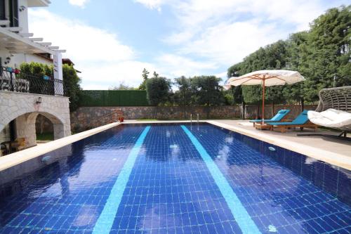 a blue swimming pool with an umbrella and two chairs and an umbrella at Villa TN - Fethiye in Fethiye