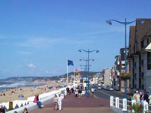 a group of people walking on a beach with the ocean at Hotel Des Falaises in Villers-sur-Mer