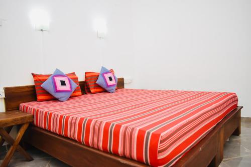 un letto con lenzuola e cuscini a righe arancioni e bianche di Weaver Bird Villa a Habarana