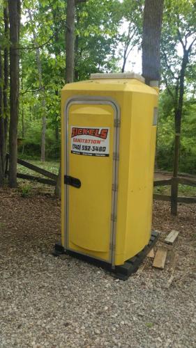 a yellow portable toilet sitting in the woods at Two Creeks Camp in Athens