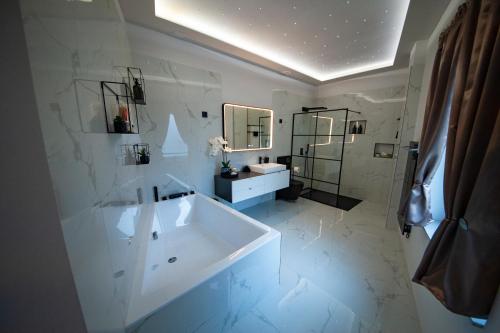 La salle de bains blanche est pourvue d'une grande baignoire et d'un lavabo. dans l'établissement Cseresznyefa Vendégház, à Dorog