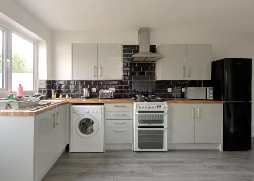 La cuisine est équipée de placards blancs et d'un lave-vaisselle. dans l'établissement Voguish 3BR Home in Huyton, à Liverpool