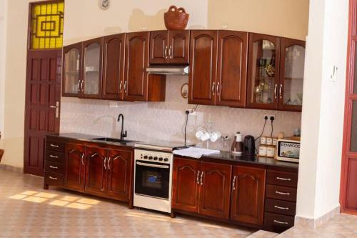 La cuisine est équipée de placards en bois et d'un four avec plaques de cuisson. dans l'établissement Hellen's Riverside villas, à Moshi