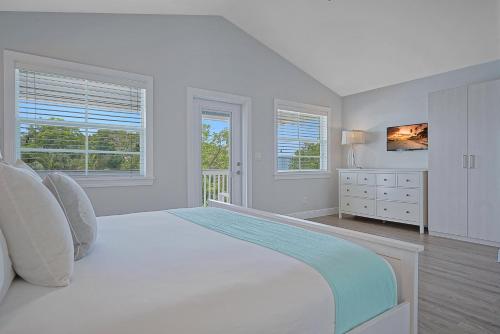 a white bedroom with a large white bed and windows at Isla Key Lime - Island Paradise, Waterfront Pool, Prime Location in Islamorada