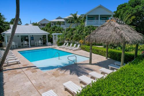 a swimming pool with chairs and a straw umbrella at Isla Key Lime - Waterfront Boutique Resort, Htd Pool, Dock, Walkable in Islamorada