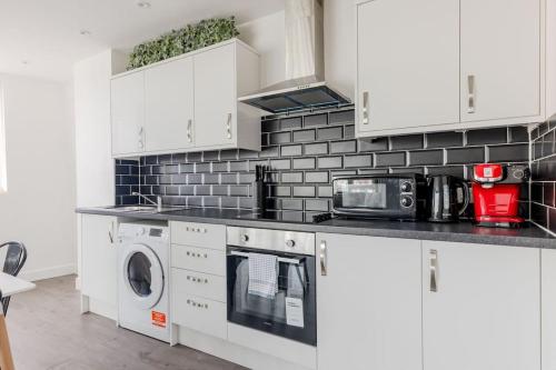 a kitchen with white cabinets and a washer and dryer at Vertigo Boutique Sleeps 4 London in Kingston upon Thames