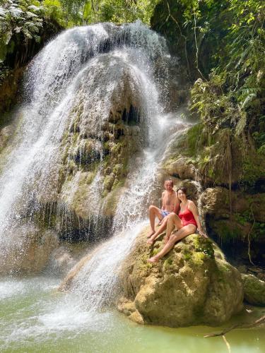 a man and woman sitting on a rock in front of a waterfall at Rancho Romana Treehouse F04 in El Limón