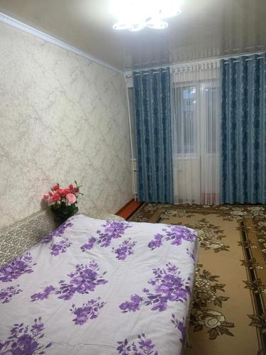 um quarto com uma cama com flores roxas em Mahabat em Karakol