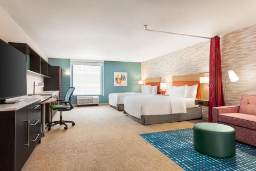 West AllisにあるHome2 Suites By Hilton Milwaukee Westのベッド、デスク、椅子が備わるホテルルームです。