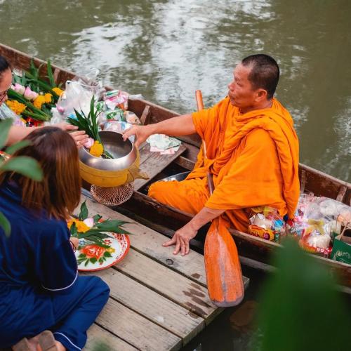 a man in an orange robe sitting in a boat at House Of Passion Amphawa in Amphawa